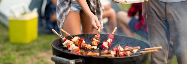 Person grillt Fleisch und Gemüse auf einem Holzkohlegrill.